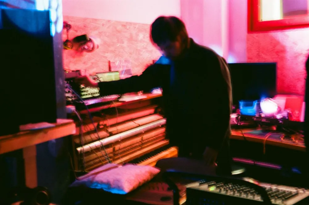 Performing at a keyboard and electronics under pink and red light.