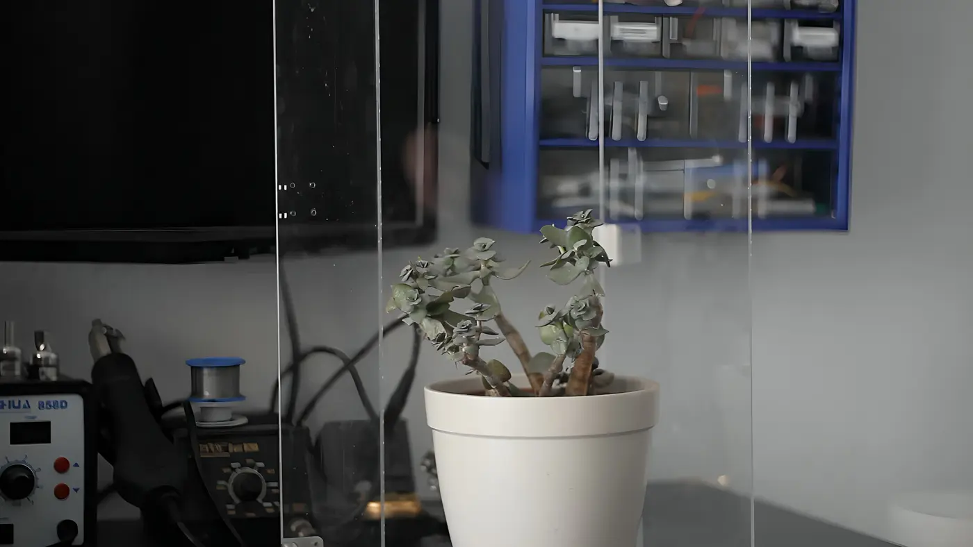 A small potted succulent behind panes of glass on a workbench with soldering equipment.