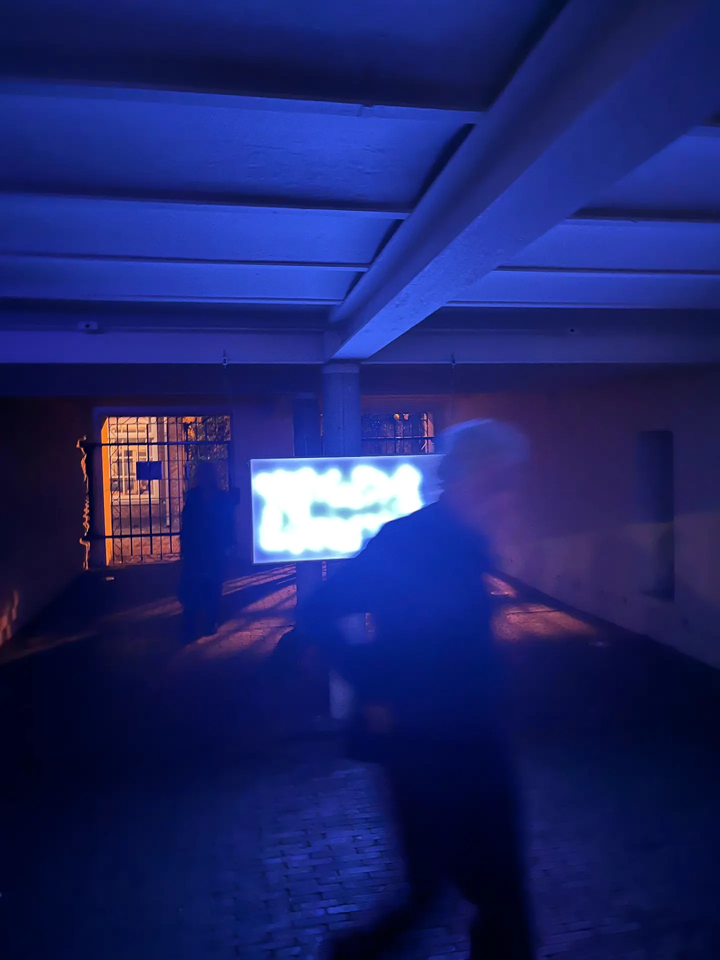 A visitor walks past the glowing LED panel in a blue-lit corridor.
